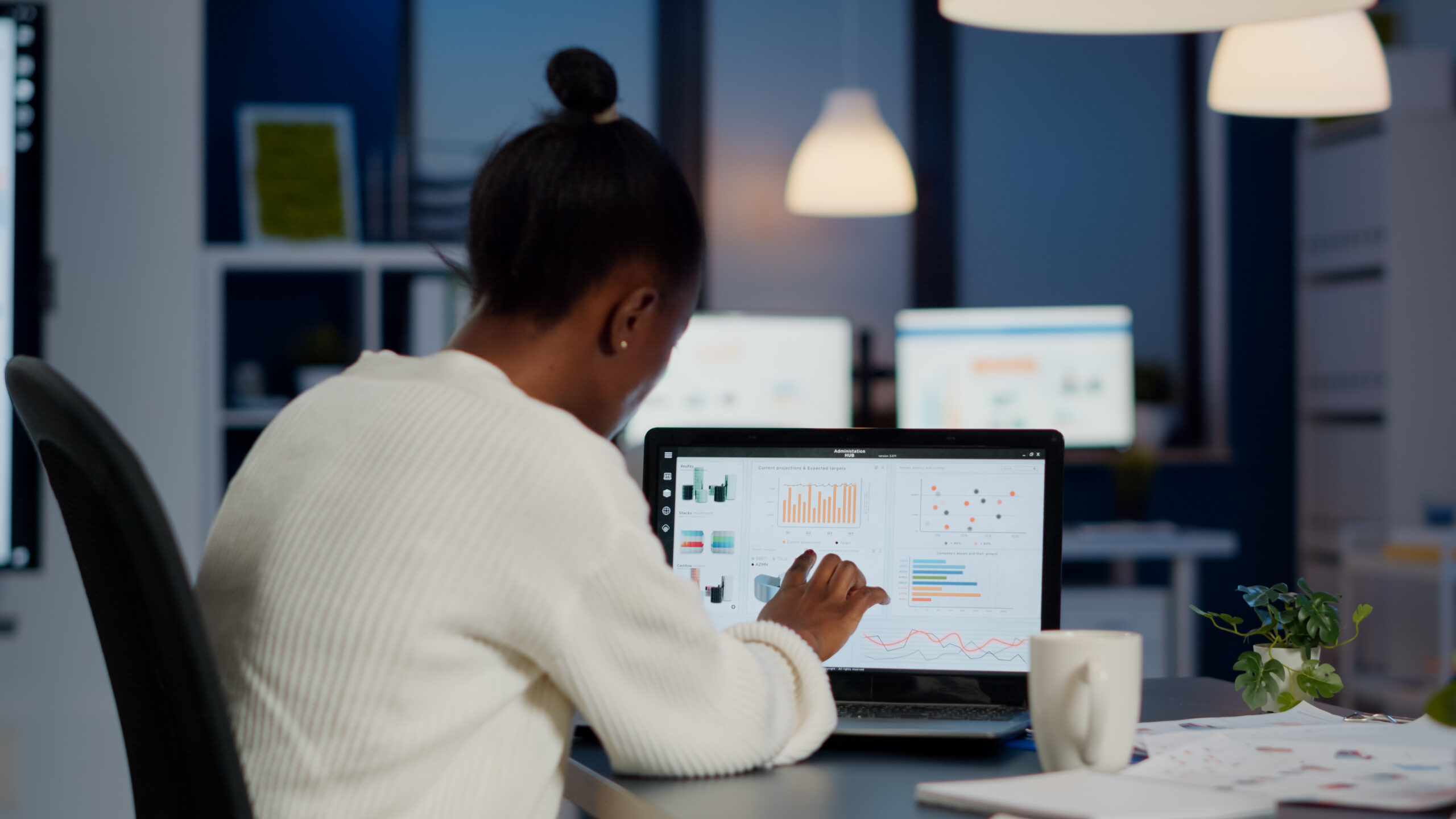 Black woman manager checking business statistics and financial reports on laptop working in start up office late at night. Focused employee doing overtime for job respecting deadline of project